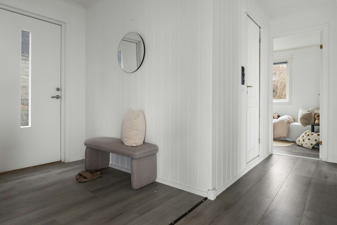 Ljus hall med sittbänk, spegel, ytterdörr och sovrum i bakgrunden
